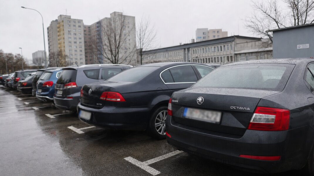 Parkovisko pred nemocnicou v Bratislave s autami a pacientmi prichádzajúcimi na vyšetrenie