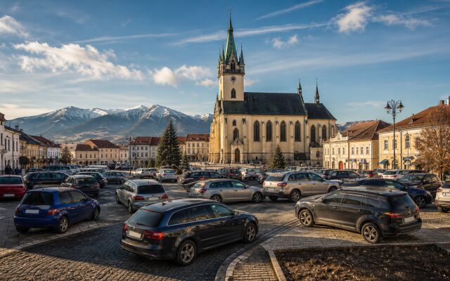 Ilustračný pohľad na Kostol svätého Mikuláša a centrum Liptovského Mikuláša s autami zaparkovanými nadivoko v popredí.
