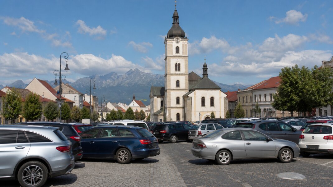 Ilustračný pohľad na Kostol svätého Egídia, centrum Popradu a Vysoké Tatry s autami zaparkovanými nadivoko v popredí.