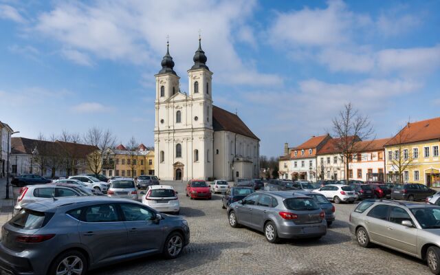 Ilustračný pohľad na historický kostol a centrum Senice s autami zaparkovanými nadivoko v popredí.