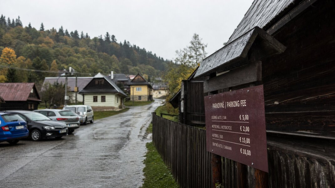 Parkovisko pri vstupe do dediny Vlkolínec s autami a turistami na prechádzke