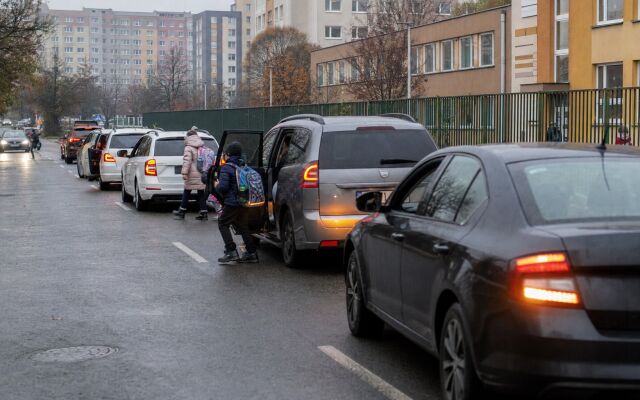 Rodič zastavuje auto pred školou, aby vysadil dieťa medzi inými vozidlami.