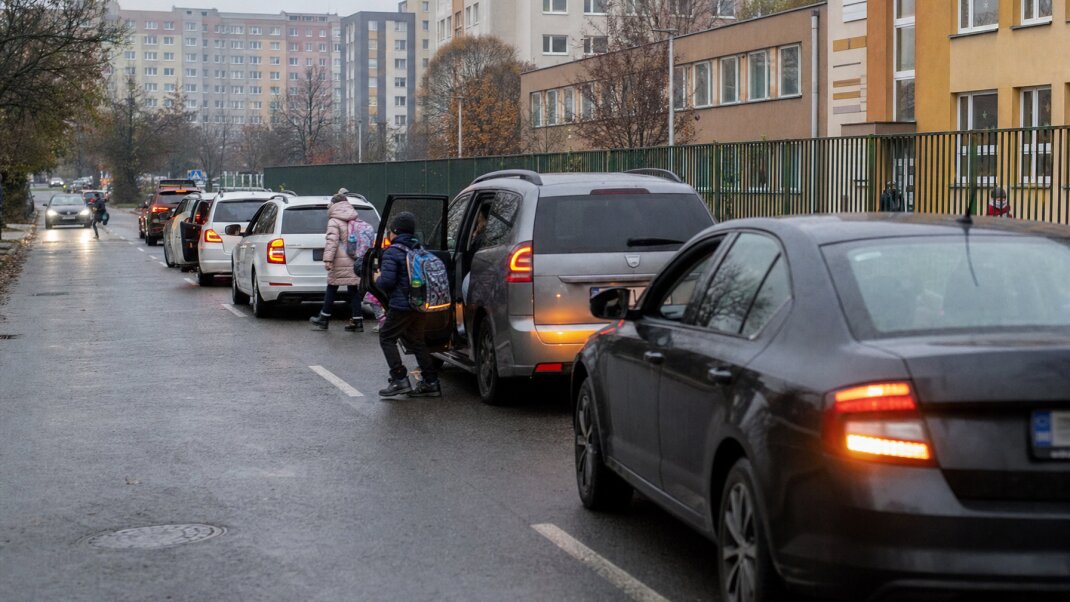 Rodič zastavuje auto pred školou, aby vysadil dieťa medzi inými vozidlami.